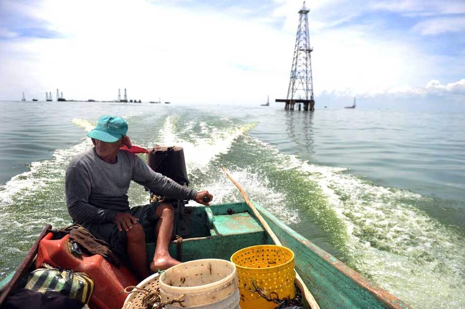 Un pescador navega frente a una torre petrolera del lago de Maracaibo , en el estado de Zulia. / AFP