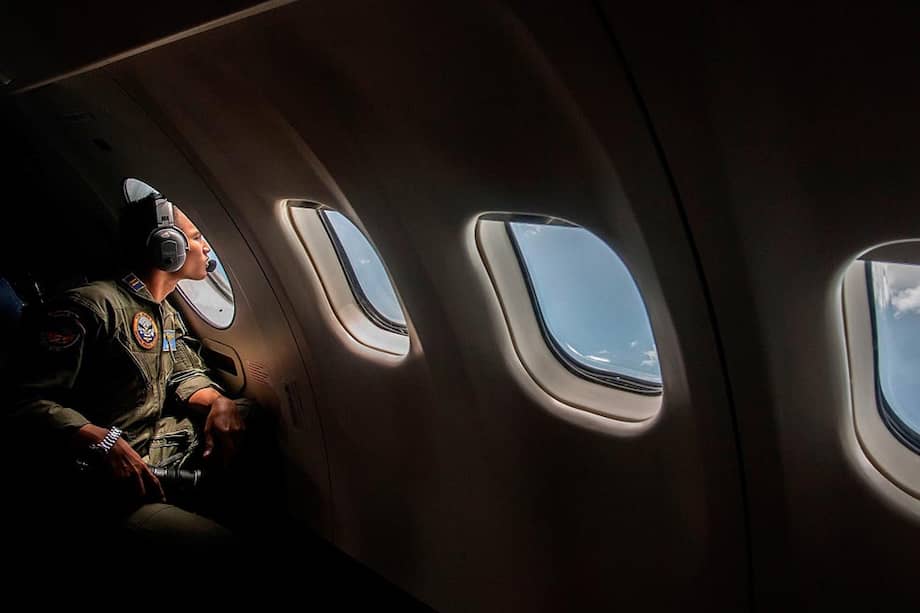 Un oficial de Indonesia mira por la ventana de uno de los aviones que participan en la búsqueda del avión de Air Asia desaparecido el domingo de los radares. / AFP