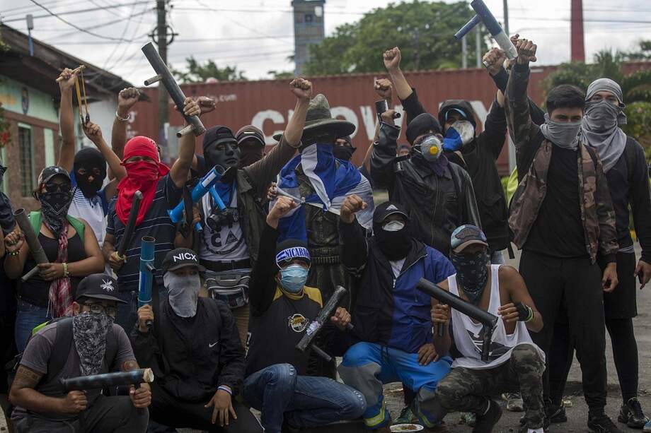 Varios jóvenes sujetan lanza morteros mientras posan junto a una estatua del héroe nacional Augusto César Sandino. / EFE