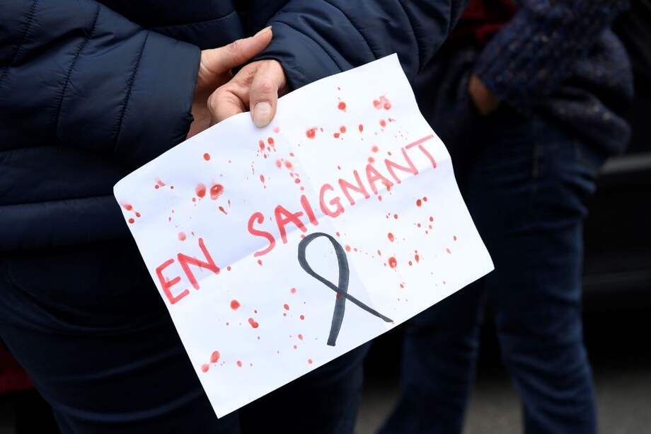 Una persona sostiene un cartel que juega con las palabras "enseigner" (enseñar) y "saignant" (sangrar) en protesta por el asesinato de un maestro en Francia.