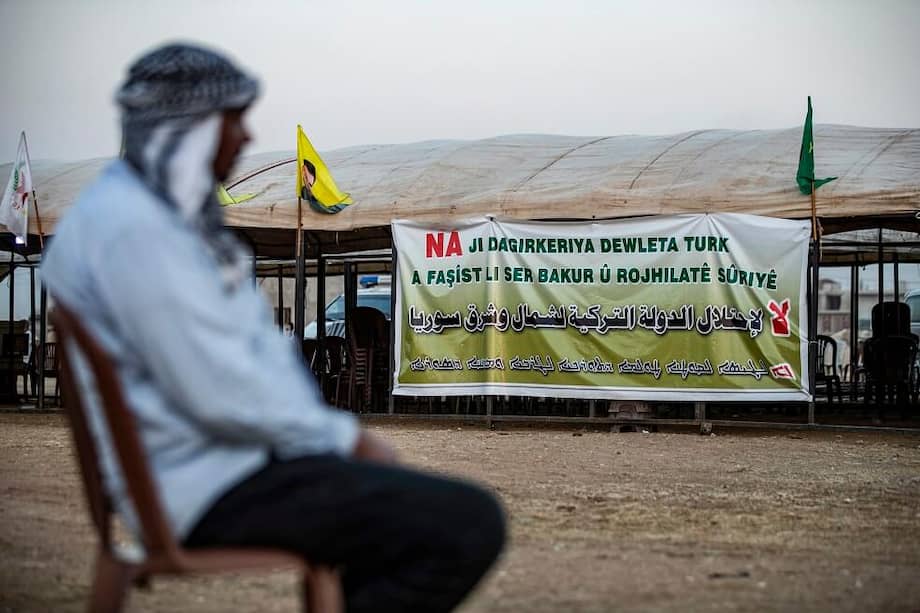 Un hombre se sienta frente a un letrero que dice en kurdo, árabe y sirio: "No a la ocupación del estado Turco en el noreste de Siria". / AFP