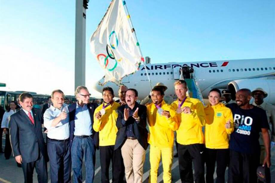 El alcalde de Río de Janeiro, Eduardo Paes, posa junto a unos atletas que ganaron medallas de plata y bronce en las olimpíadas de Londres 2012, a su llegada con la bandera olímpica. / EFE