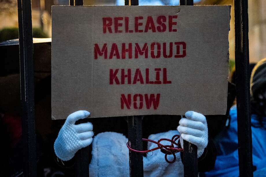 Un estudiante de la Universidad de Columbia, encadenado a la valla, sostiene un cartel que dice "Liberen a Mahmoud Khalil".