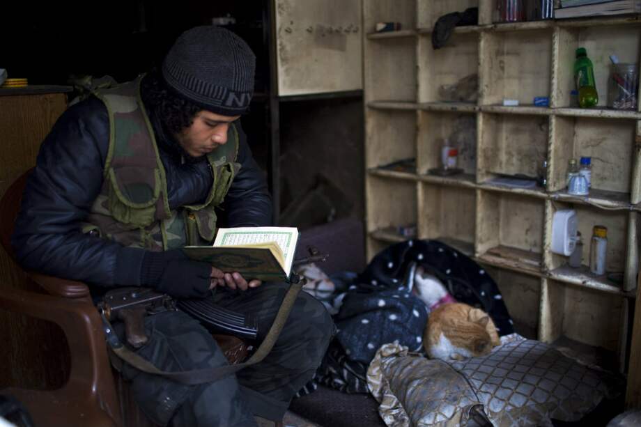 Un rebelde sirio hace una pausa en los enfrentamientos para leer el Corán en el comienzo de 2013. / AFP
