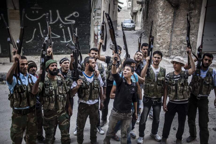 Rebeldes sirios levantan sus armas frente a un edificio recién bombardeado/ EFE