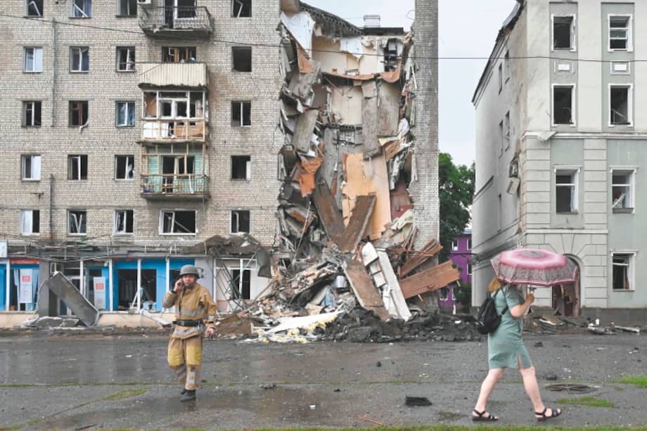 Un residente local pasa junto a un rescatista que trabaja afuera de un edificio atacado con misiles rusos en Járkov el 11 de julio de 2022.