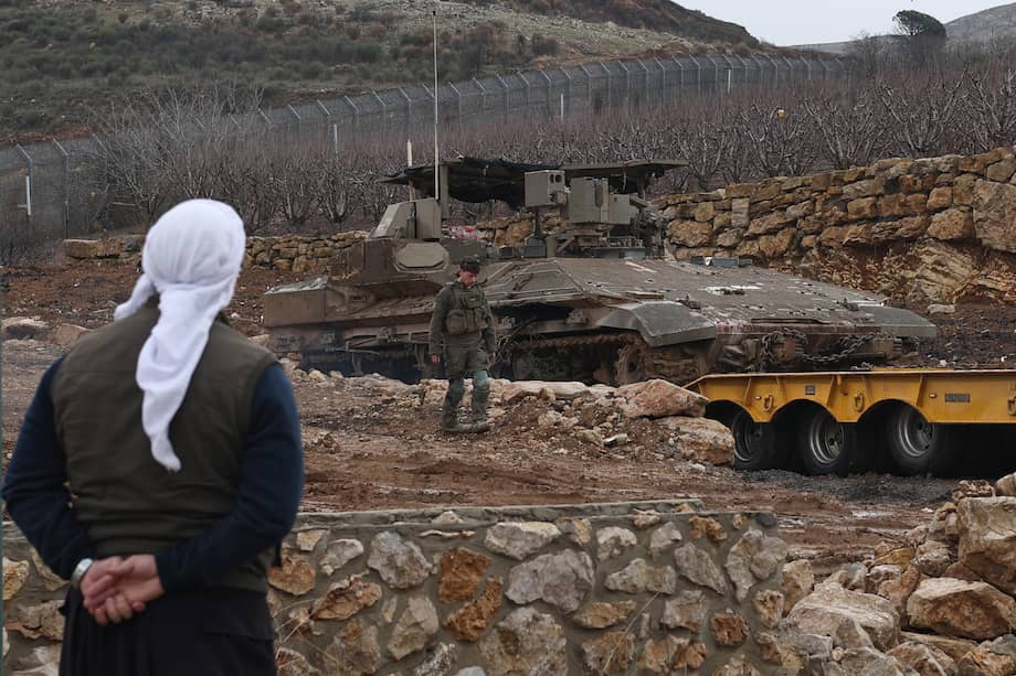 Un druso observa un soldado israelí y un vehículo blindado de transporte de tropas (APC) en un camión mientras los soldados salen de la zona de amortiguación, en la frontera entre Israel y Siria, cerca de la aldea drusa de Majdal Shams.