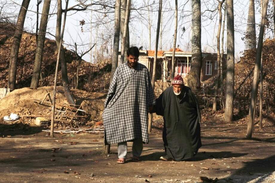 El empresario Sabzar Khan, que ha puesto a la venta su riñón, camina con su padre discapacitado Ghulam Hassan frente a su casa en una aldea de India.