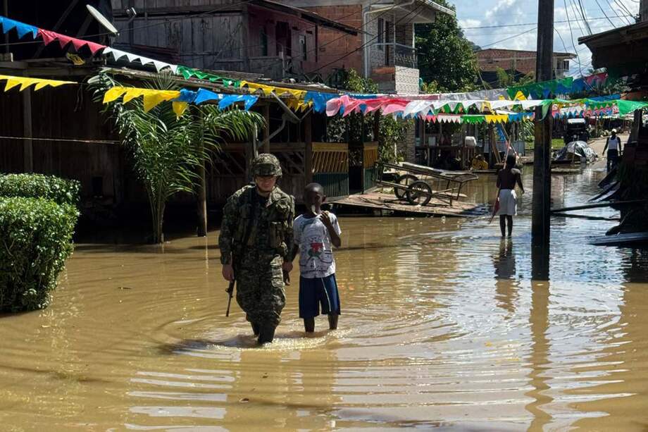 Un solado acompaña a un joven por una calle inundada en Alto Baudó, donde las lluvias han dejado más de 7.000 damnificados.