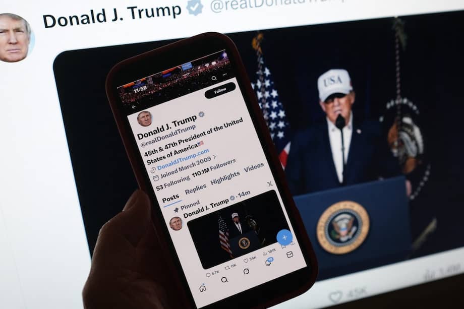 Esta imagen ilustrativa muestra a una persona mirando un teléfono inteligente que muestra al presidente estadounidense Donald Trump haciendo una declaración sobre las operaciones de combate en Irán, junto a una pantalla de computadora con el mismo mensaje publicado el 28 de febrero de 2026 en X.