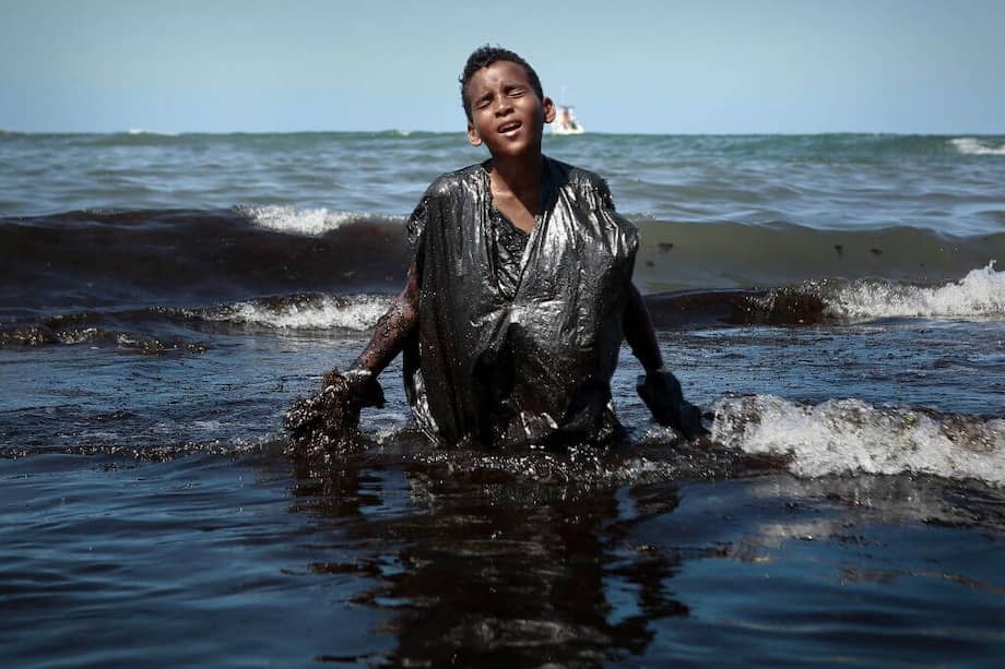Niño ayudando a retirar petróleo en la playa Itapuama de ciudad abo de Santo Agostinho, en octubre de 2019. / AFP