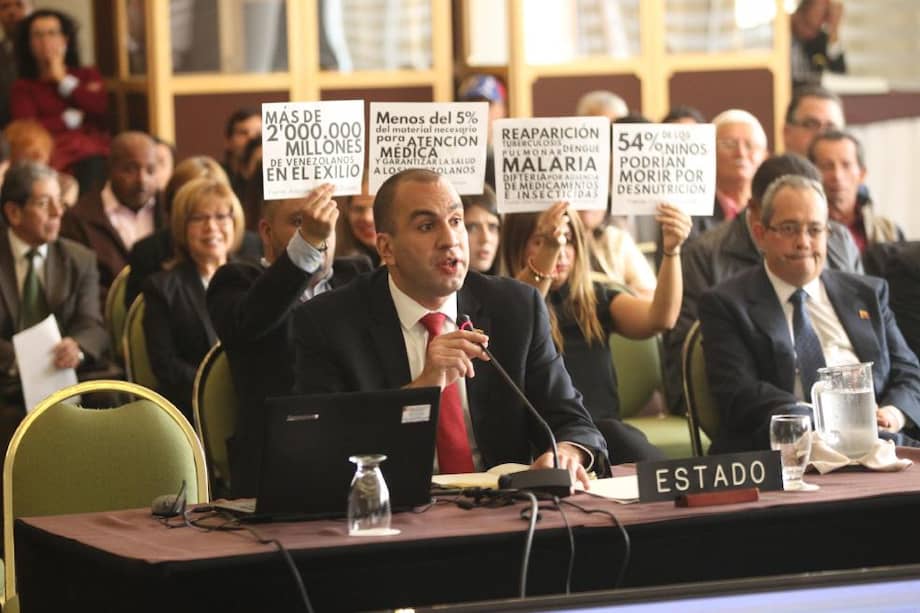 El representante del Estado Venezolano, Larry Devoe, responde a miembros de la Comisión Interamericana de Derechos Humanos (CIDH), mientras asistentes a la audiencia pública "Derecho a la alimentación y a la salud de Venezuela", protestan contra el Gobierno de Caracas en febrero de 2018.