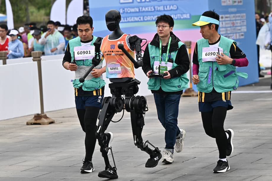 Un robot y sus ingenieros corren la media maratón de robots humanoides en Pekín el 19 de abril de 2025. Decenas de robots humanoides salieron a las calles de Pekín, uniéndose a miles de sus homólogos de carne y hueso en una primera media maratón mundial que demuestra el afán de China por liderar la carrera mundial en tecnología de vanguardia.