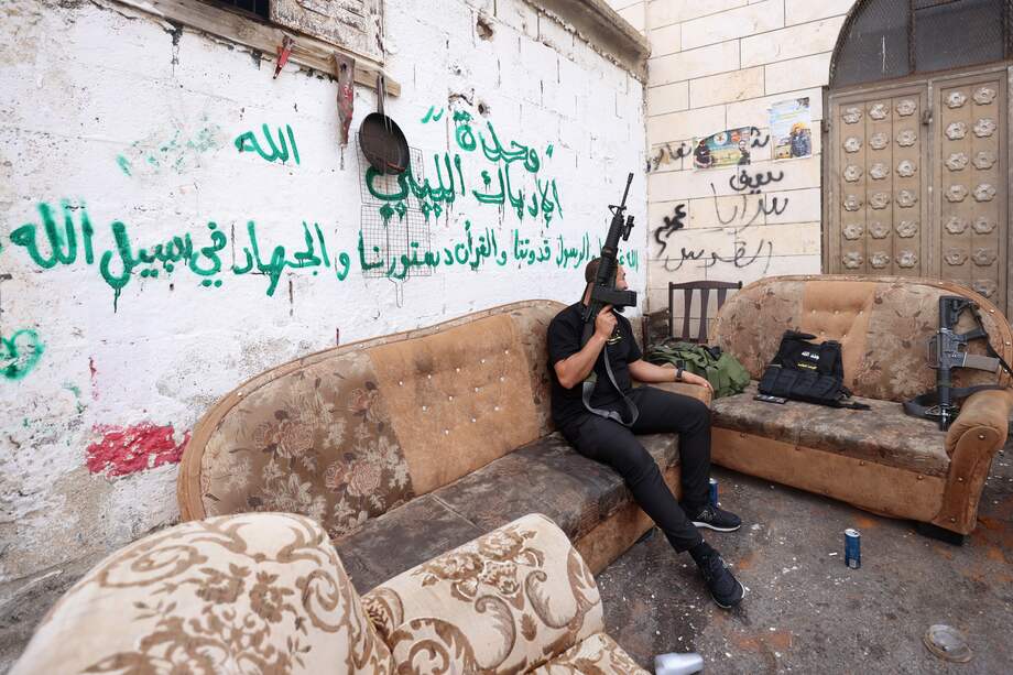 Un palestino agarra su fusil mientras espera sentado en un sofá antes de asistir al funeral por el palestino de 66 años Gazi Shihab, muerto en una redada del Ejército israelí en el campo de refugiados de Nur Shams.