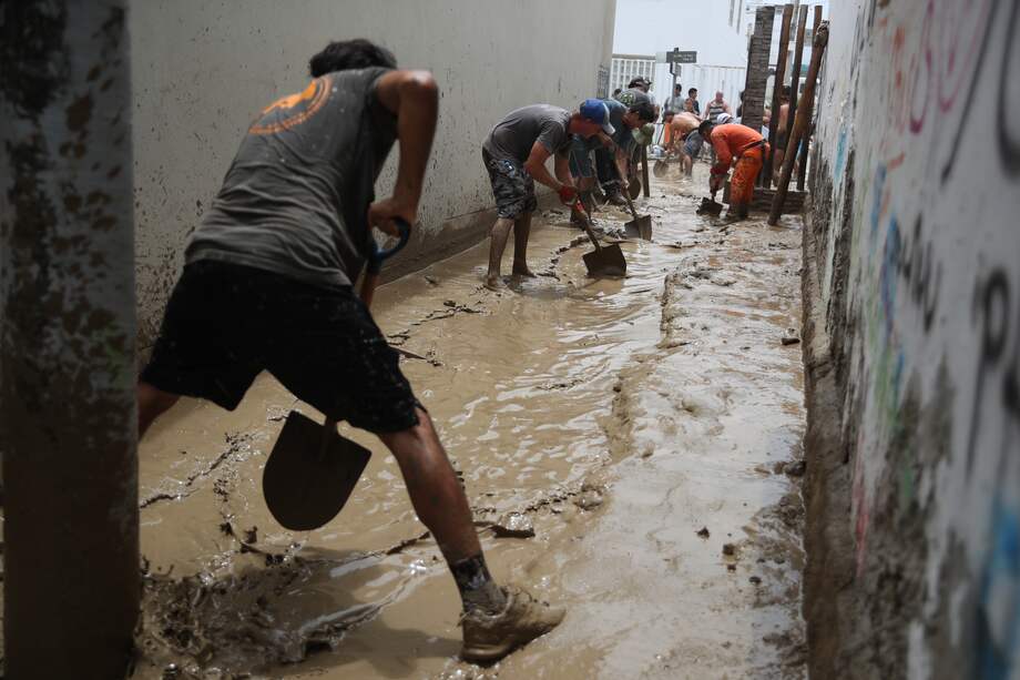 Personas ayudan a remover el lodo en una calle afectada por las lluvias hoy, en el balneario de Punta Hermosa al sur de Lima.