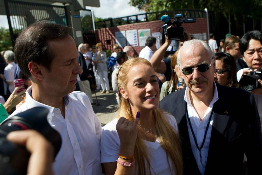 La esposa del político opositor venezolano Leopoldo López, Lilian Tintor muestra su dedo después de votar acompañada del expresidente de Colombia Andrés Pastrana. / EFE