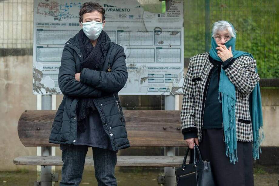 Dos mujeres se cubren la boca mientras esperan su autobús durante el primer día de medidas de confinamiento en el archipiélago de Azores en Ponta Delgada, Isla de Sao Miguel, Portugal. / EFE