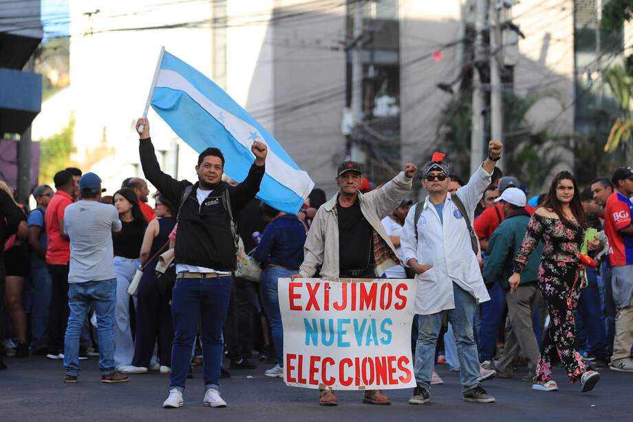 Personas sostienen carteles y banderas frente al Congreso Nacional durante una sesión extraordinaria este jueves, en Tegucigalpa (Honduras).