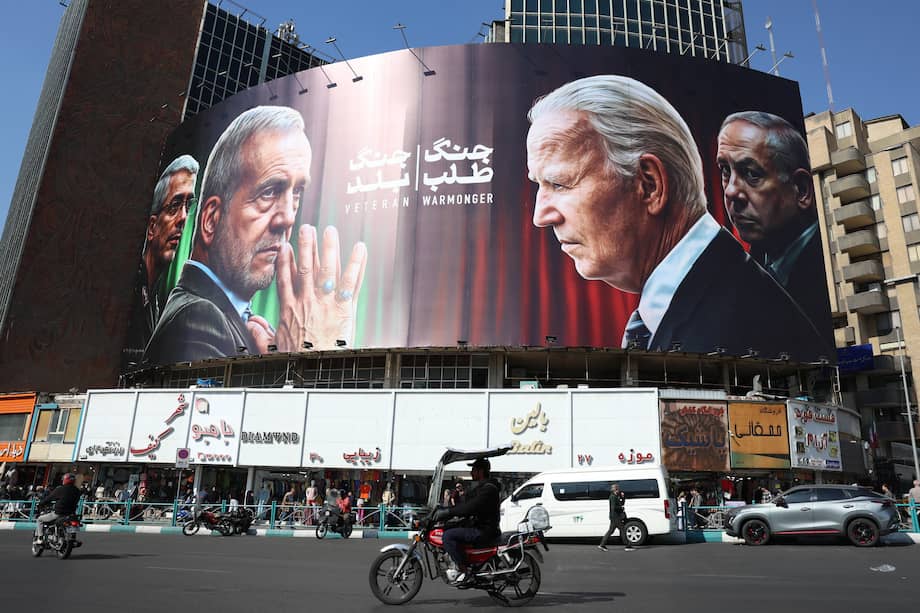 Iraníes pasan por un edificio decorado con un cartel contra Israel con las imágenes del presidente, Masoud Pezeshkian, y comandante general de la Guardia Revolucionaria, Mohammad Bagheri (i), el presidente de EEUU, Joe Biden, y el de Israel, Benjamin Netanyahu, en la plaza de Valiasr en Teherán.