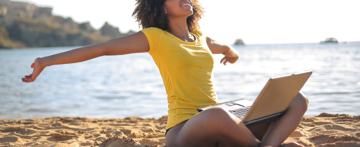 Young woman sitting at the beach, using her laptop