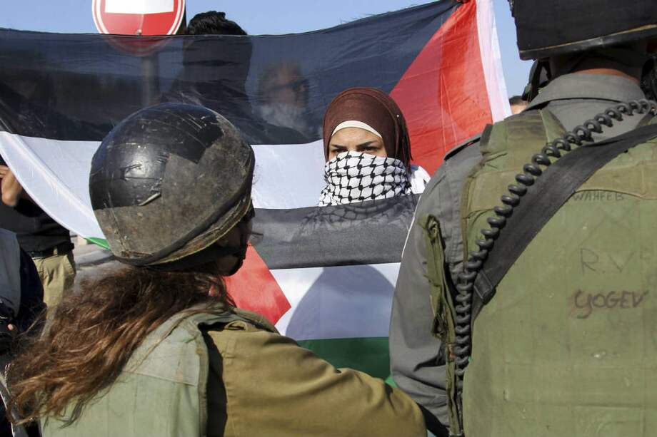 Los bombardeos israelíes a Gaza han generado protestas en territorio ocupado. Una mujer sostiene la bandera palestina enfrente de militares hebreos. / EFE