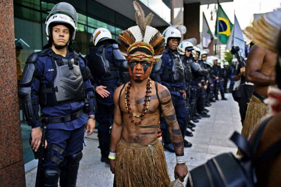En esta fotografía de abril 25 de 2018, un indígena atraviesa una concentración de policías antidisturbios en Brasilia, en el marco de protestas por la decisión del gobierno de no reconocer la demarcación de la reserva indígena Raposa Serra do Sol, en el estado de Roraima. / CARL DE SOUZA / AFP