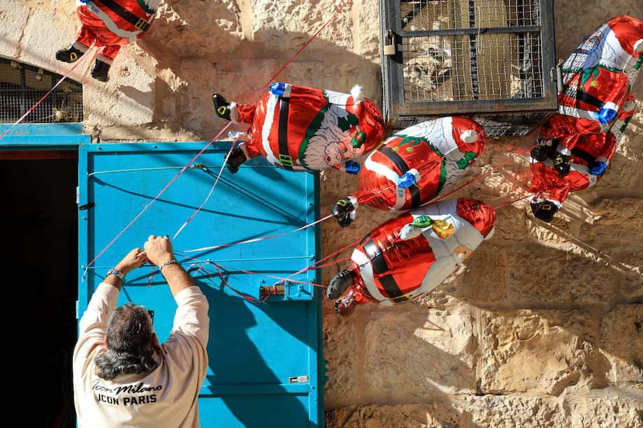 Un palestino coloca globos navideños en las puertas de su negocio durante el tradicional desfile de Navidad por las calles de Belén, Cisjordania.
