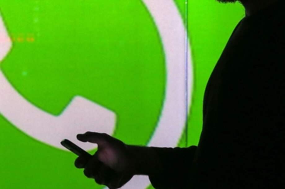 People are seen as silhouettes as they check mobile devices whilst standing against an illuminated wall bearing WhatsApp Inc's logo in this arranged photograph in London, U.K., on Tuesday, Jan. 5, 2016. WhatsApp Inc. offers a cross-platform mobile messaging application that allows users to exchange messages. Photographer: Chris Ratcliffe/Bloomberg