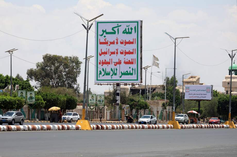 Los vehículos pasan junto a una valla publicitaria que muestra un lema hutí que dice en árabe: "Muerte a Estados Unidos, muerte a Israel, una maldición a los judíos, victoria para el Islam".