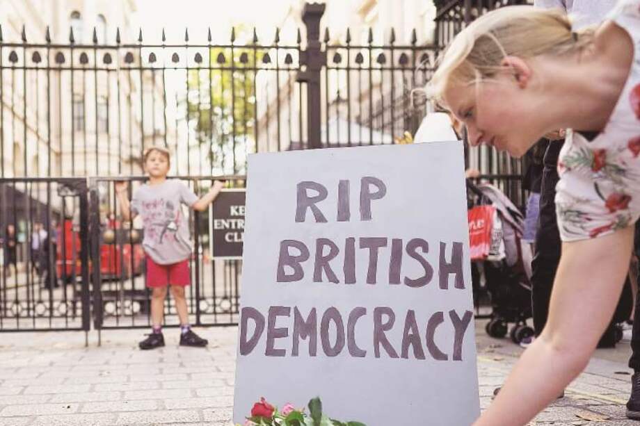 Una mujer deja unas flores frente a una tumba en la que se lee “Descanse en paz la democracia británica”. / EFE