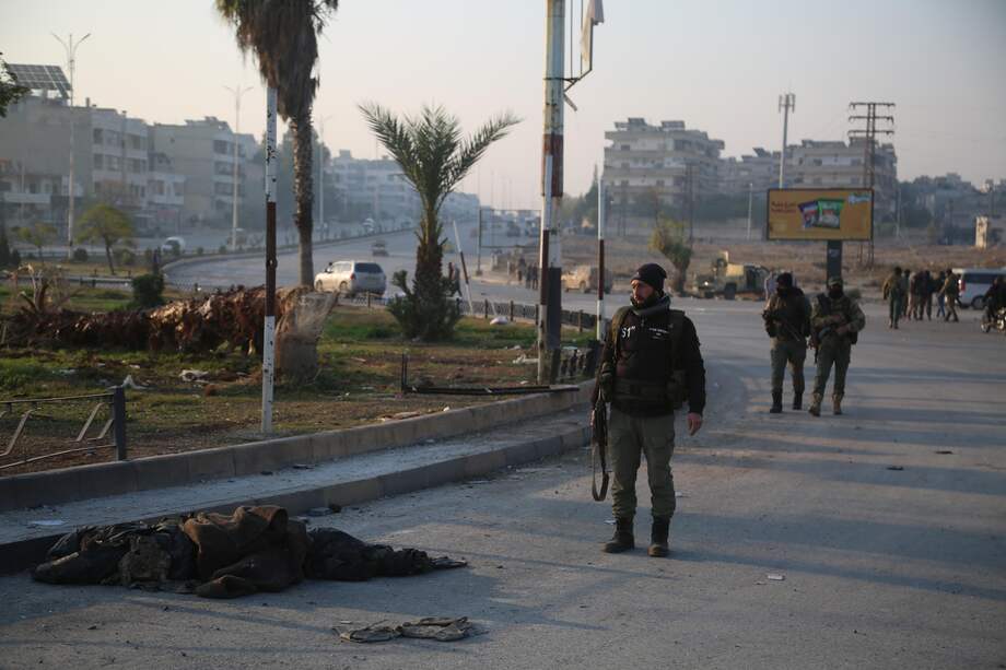 Combatientes de la oposición caminan cerca del cuerpo cubierto de un soldado sirio después de que ingresaran a la ciudad de Hama, Siria, el 06 de diciembre de 2024.