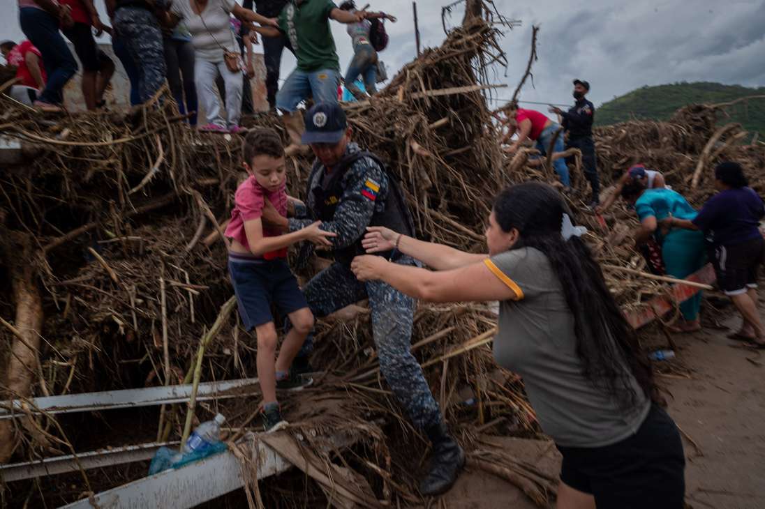 AME3286. TEJERIAS (VENEZUELA), 09/10/2022.- Un policía ayuda a un niño a sobrepasar obstáculos tras las lluvias y desbordamiento de la quebrada (rio) Los Patos, hoy en Las Tejerias (Venezuela). La crecida de una quebrada este sábado arrastró viviendas, mobiliario urbano, e inundó las calles de la localidad, arrasando con todo lo que el agua encontró a su paso. El Gobierno desplegó hoy organismos de salvamento, seguridad ciudadana, así como cuadrillas de mantenimiento y limpieza, y personal de diversas instituciones para "la atención integral del pueblo", dijo el presidente Nicolás Maduro a través de su cuenta de Twitter.EFE/ Rayner Peña R.