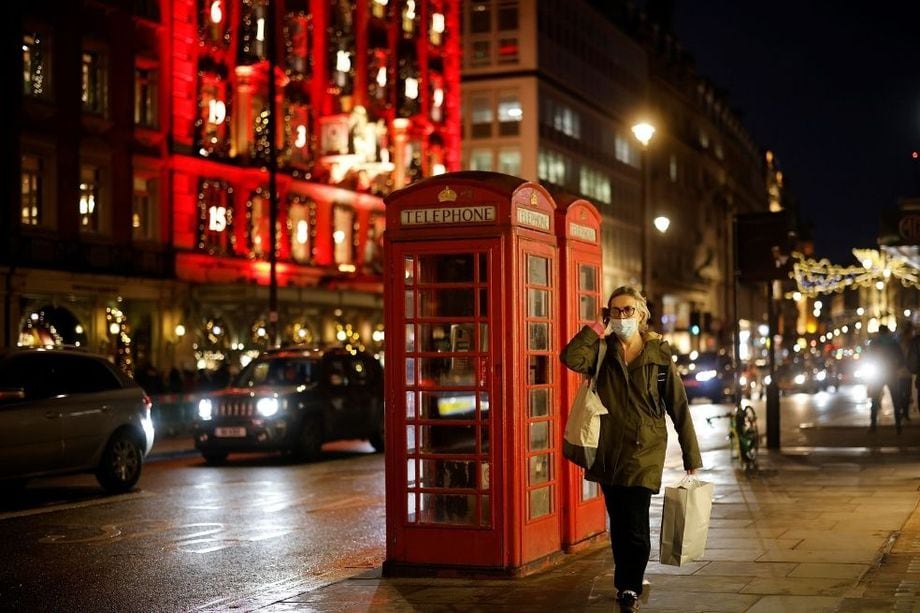 Una mujer que lleva una tapabocas pasa frente a las populares cabinas telefónicas rojas de Londres en Inglaterra.