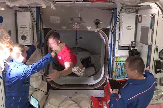 Miembros de la tripulación de la nave espacial SpaceX Crew Dragon (de rojo) son recibidos en la Estación Espacial Internacional.