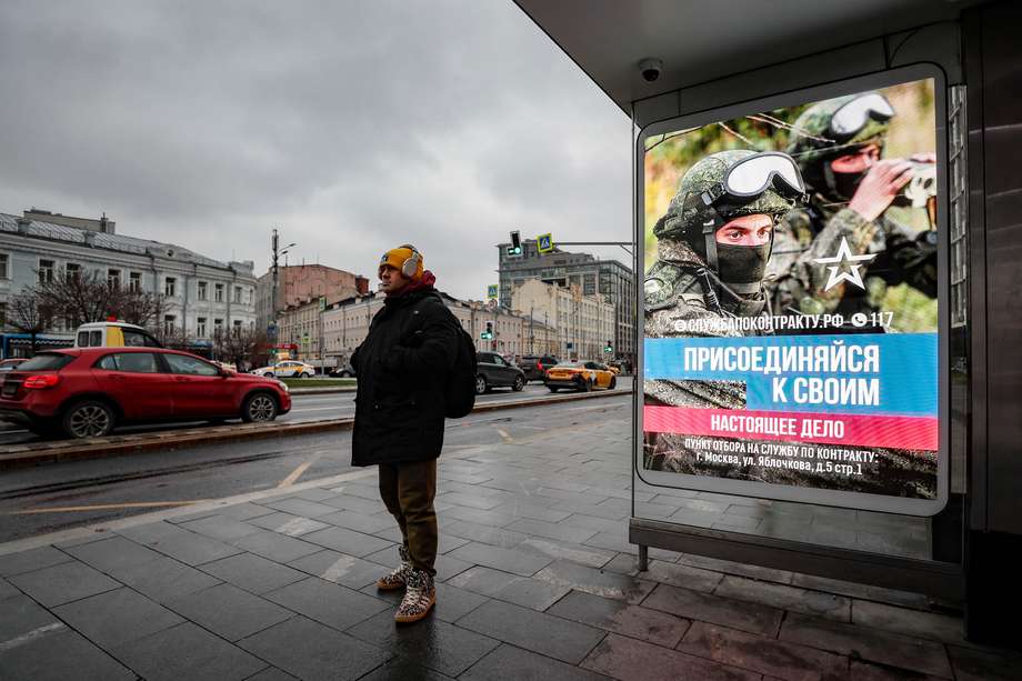 Un hombre espera el autobús en una parada en la que se anuncia el reclutamiento militar, mostrando a un soldado ruso y el mensaje "Únete a los tuyos. El verdadero trabajo' en una pantalla electrónica en Moscú, Rusia.