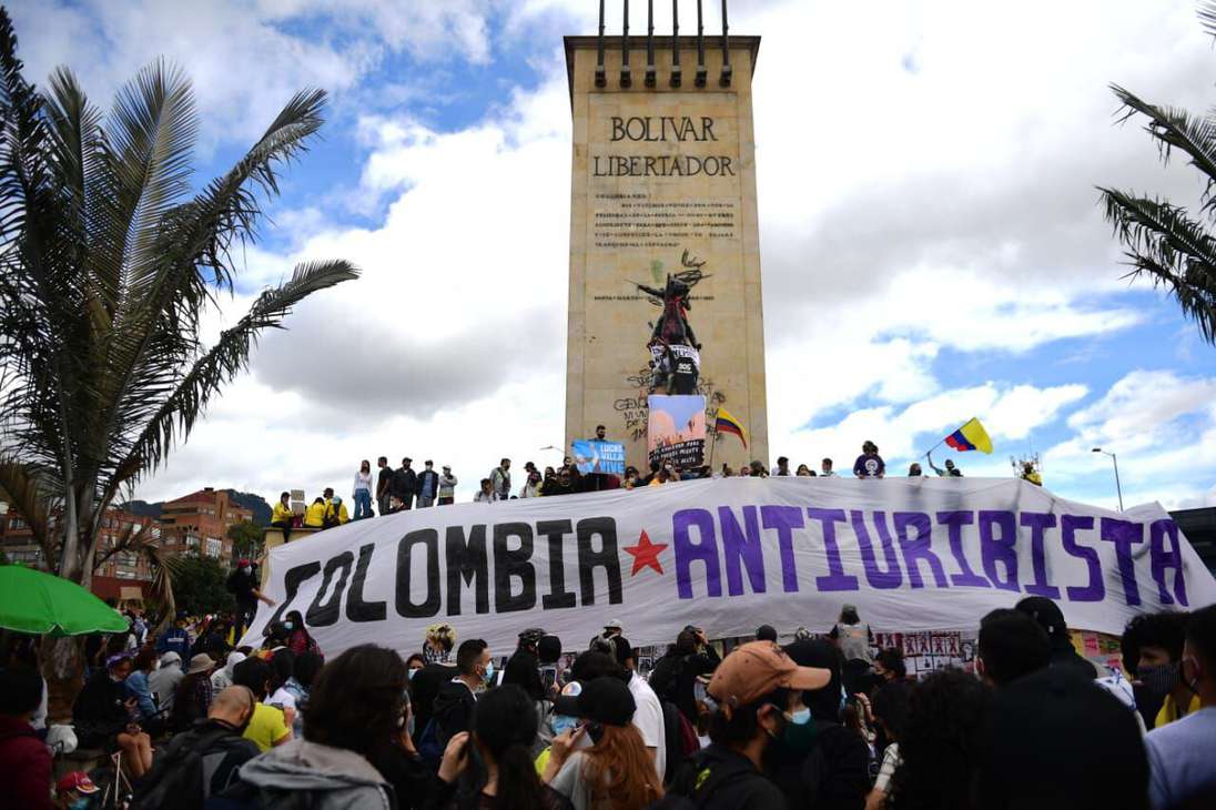 El monumento a Héroes. Al frente varias personas con una bandera que dice Colombia antiuribiste