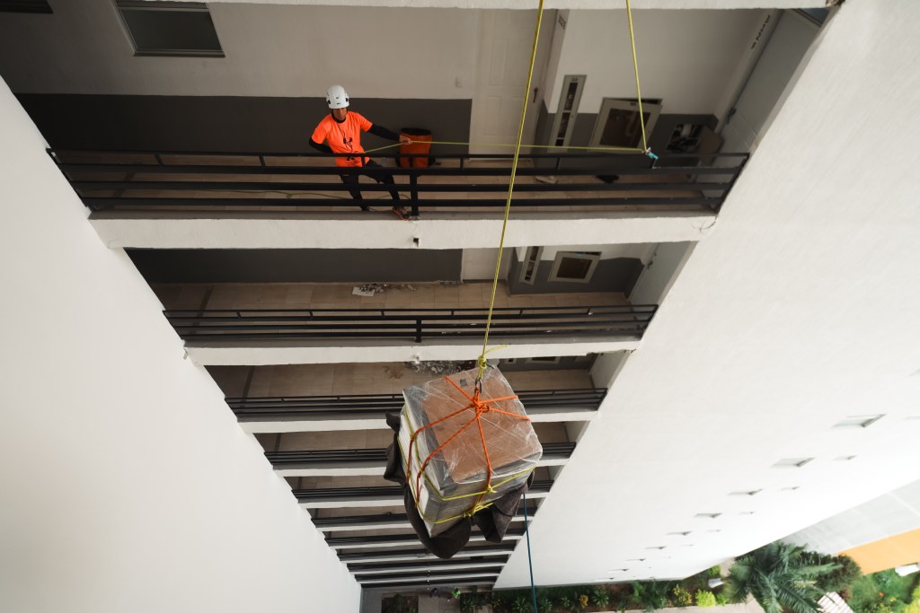 A más de 40 metros de altura, Sergio Castañeda y Roberto Gómez utilizan cuerdas y una polea para bajar una nevera hasta el primer piso de un edificio en riesgo de colapso.