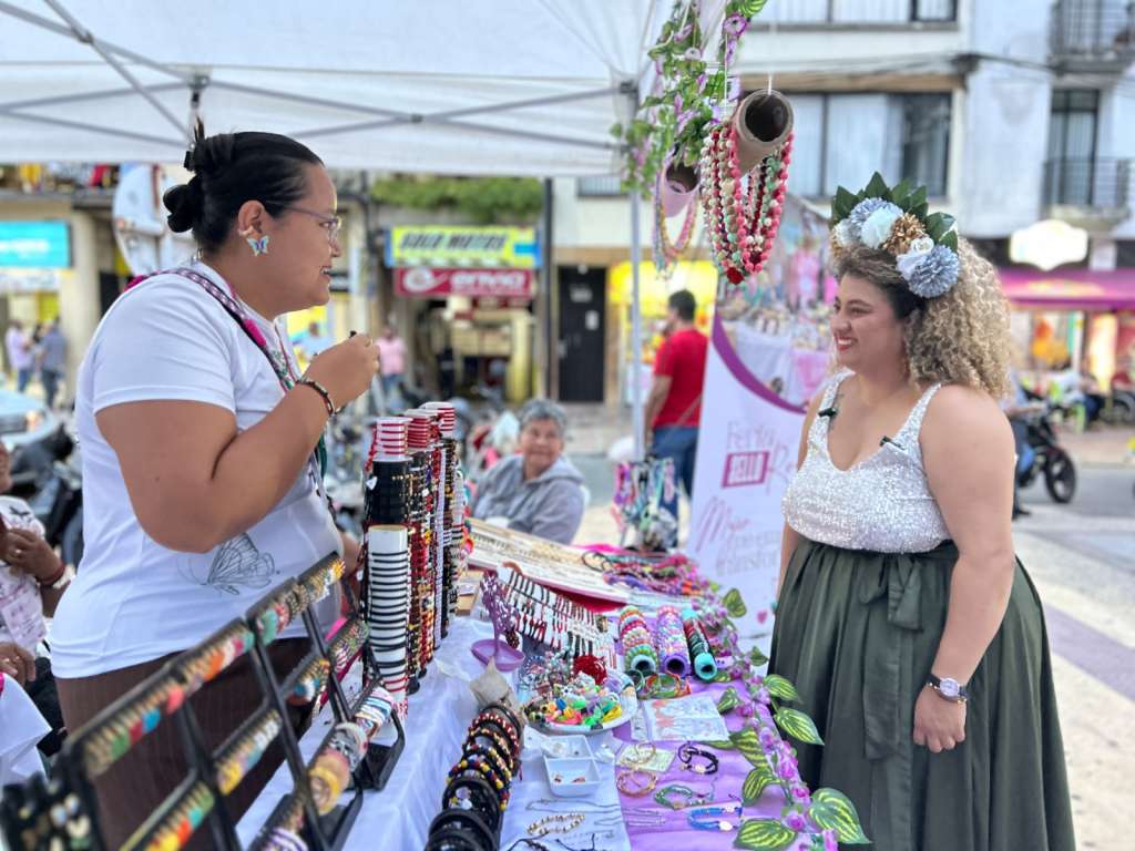Juanita Espeleta, secretaria de Desarrollo de Caldas, sonríe mientras conversa con una artesana en un puesto de feria, promoviendo la reactivación económica en Caldas.