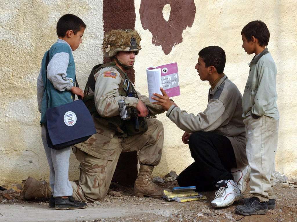 Un soldado estadounidense del batallón 1-22 de la 4.ª División de Infantería observa un libro de inglés junto a escolares iraquíes durante una patrulla en Tikrit, Irak.