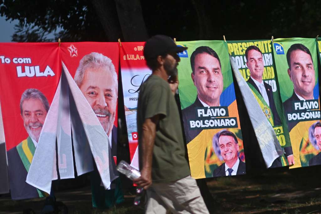 AME1288. BRASILIA (BRASIL), 30/09/2026.- Un hombre camina frente a una tienda informal de banderas con la imagen del presidente de Brasil y candidato a la reelección, Luiz Inácio Lula da Silva y del candidato presidencial, Flávio Bolsonaro, este lunes en Brasilia (Brasil). Mientras las encuestas hablan de una extrema igualdad entre el presidente progresista Luiz Inácio Lula da Silva y el ultraderechista Flávio Bolsonaro, analistas consideran que el resultado de las elecciones brasileñas del 4 de octubre depende de un amplio sector que observa el proceso con distancia y escepticismo: los indecisos. EFE/Andre Borges
