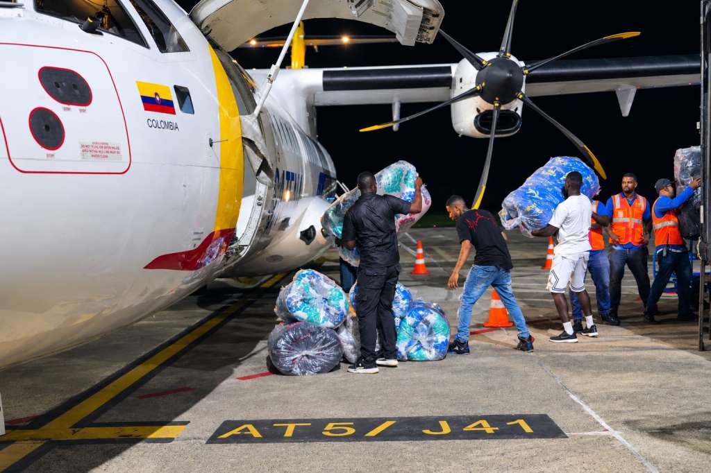 Equipo de apoyo carga paquetes envueltos en plástico dentro de un avión colombiano durante un vuelo humanitario nocturno en la pista.
