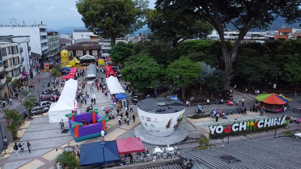 Vista aérea del Parque Bolívar de Chinchiná durante la jornada de reactivación económica en Caldas, mostrando carpas de emprendedores, el letrero "YO ❤️ CHINCHINÁ" y el monumento a la taza de café.