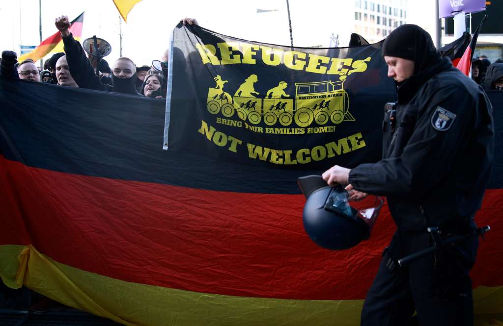 BERLIN (Germany), 22/02/2025.- A police officer walks past participants shouting slogans and displaying a flag and banner during a demonstration by right-wing protesters against 'left-wing extremism' in Berlin, Germany, 22 February 2025. (Protestas, Alemania) EFE/EPA/CLEMENS BILAN