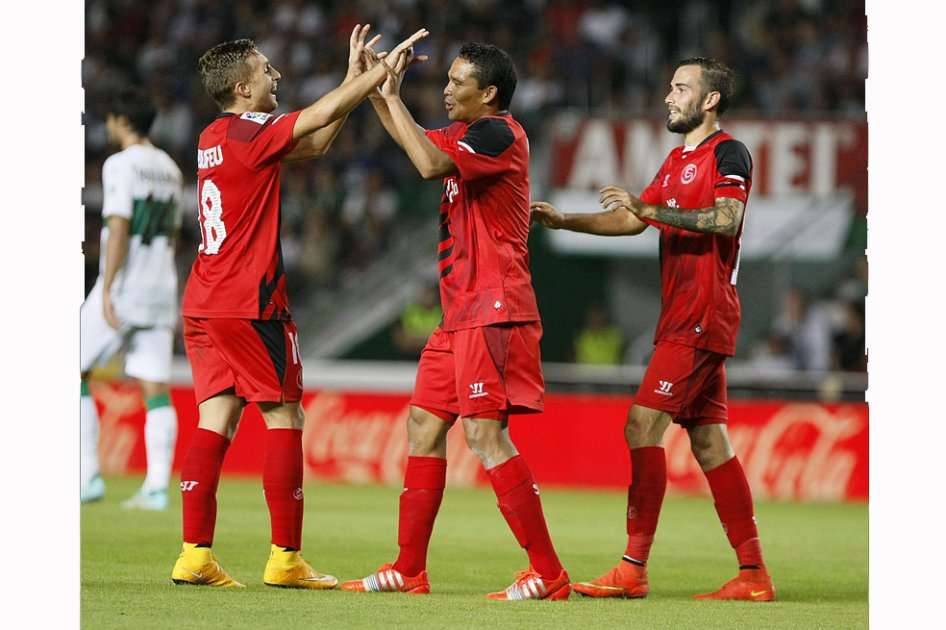 El delantero colombiano del Sevilla Carlos Bacca (c) es felicitado por Deulofeu (i) tras marcar el primer gol ante el Elche, durante el partido de la octava jornada de la Liga en Primera División que disputan esta tarde en el estadio Martínez Valero. / EFE/Manuel Lorenzo