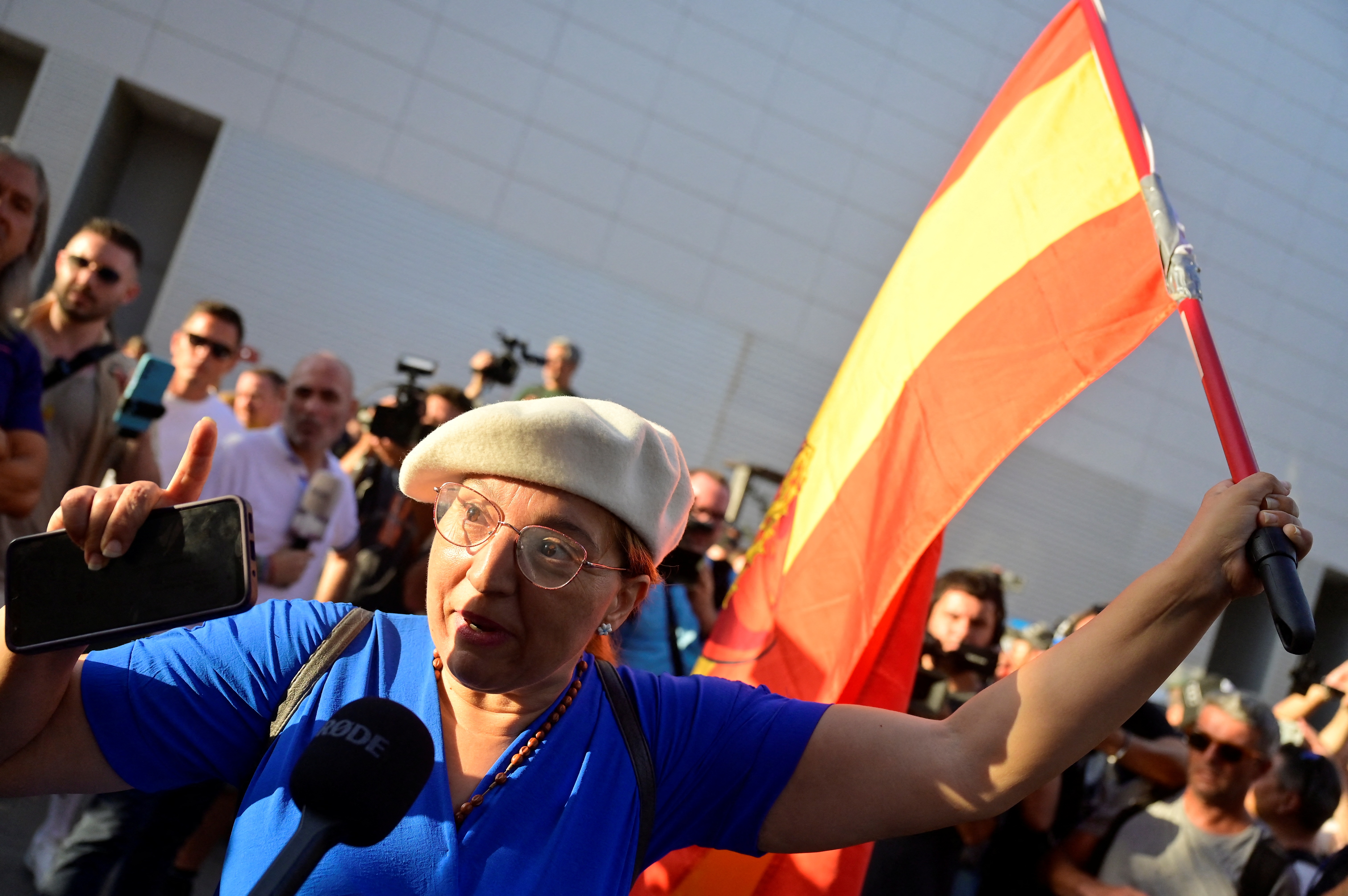 Una mujer con una bandera española habla con los medios de comunicación durante una manifestación convocada por grupos de extrema derecha contra los migrantes.