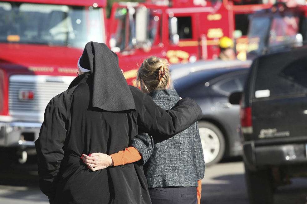 Una monja y una mujer caminan abrazadas en las afueras de la escuela Sandy Hook , escenario de una matanza ejecutada por un fanático de los videojuegos. / EFE