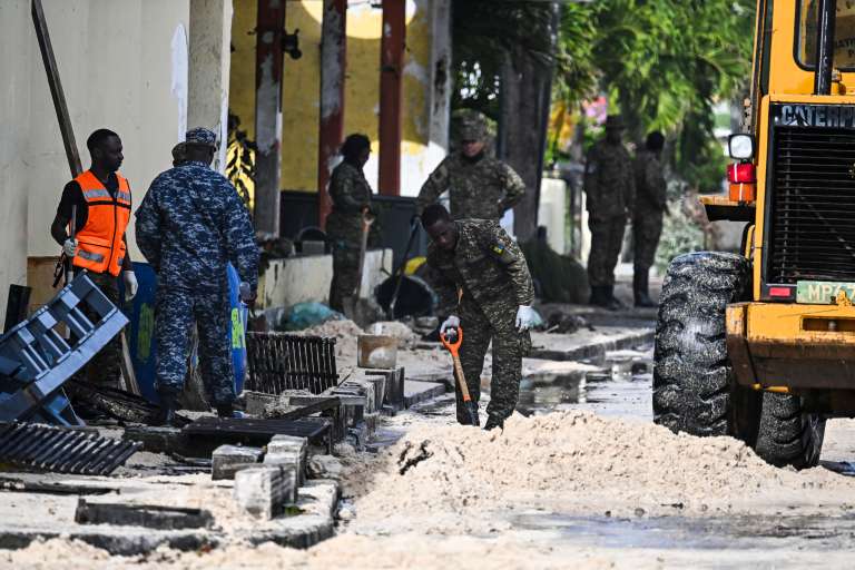 Miembros de las Fuerzas Armadas Nacionales de Barbados limpian de arena una calle inundada por el agua del mar.
