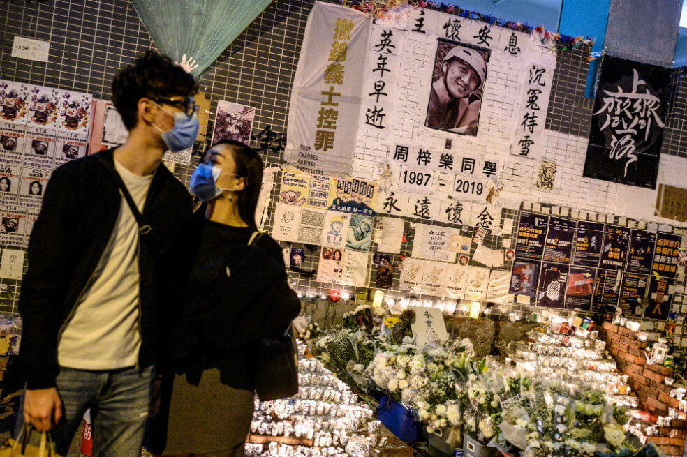 Dos jóvenes presentan sus condolencias a Alex Chow, de 22 años, quien murió hace dos meses por heridas en la cabeza sufridas durante una caída dentro de un estacionamiento de varios pisos donde la policía y los manifestantes se enfrentaban. / AFP
