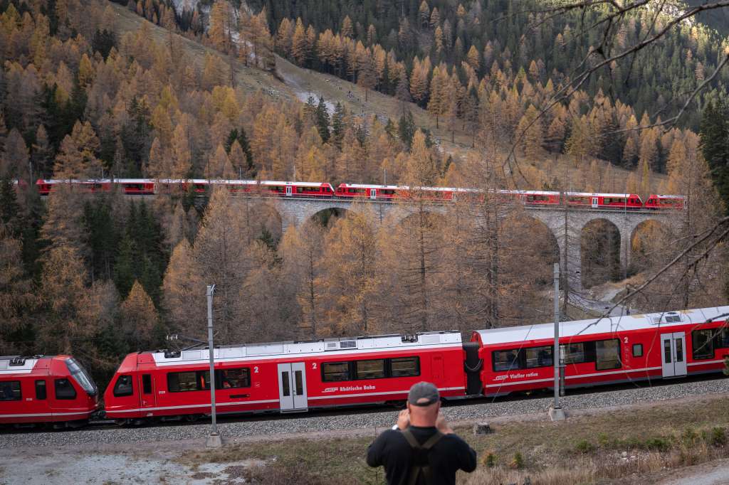 A member of the public captures images as a 1910-metre-long train with 100 cars passes near Bergun, on October 29, 2022, during a record attempt by the Rhaetian Railway (RhB) of the World's longest passenger train, to mark the Swiss railway operator's 175th anniversary. - The record attempt is carried out on the Albula Line, from Preda to Thusis, crossing one of the most spectacular railways in the world, recognised as a Unesco World Heritage Site. (Photo by Fabrice COFFRINI / AFP)