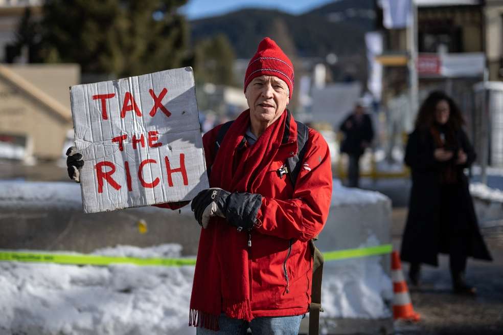 Phil White, millonario británico, posa con una pancarta en la que se lee: "Impuestos a los ricos" junto al centro de congresos durante la reunión anual del Foro Económico Mundial (FEM). / AFP